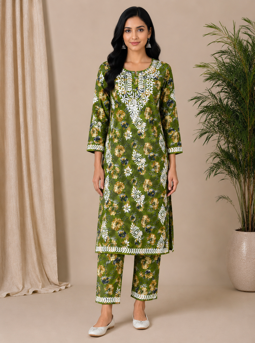 Woman wearing a green floral traditional outfit against a beige curtain and plant background